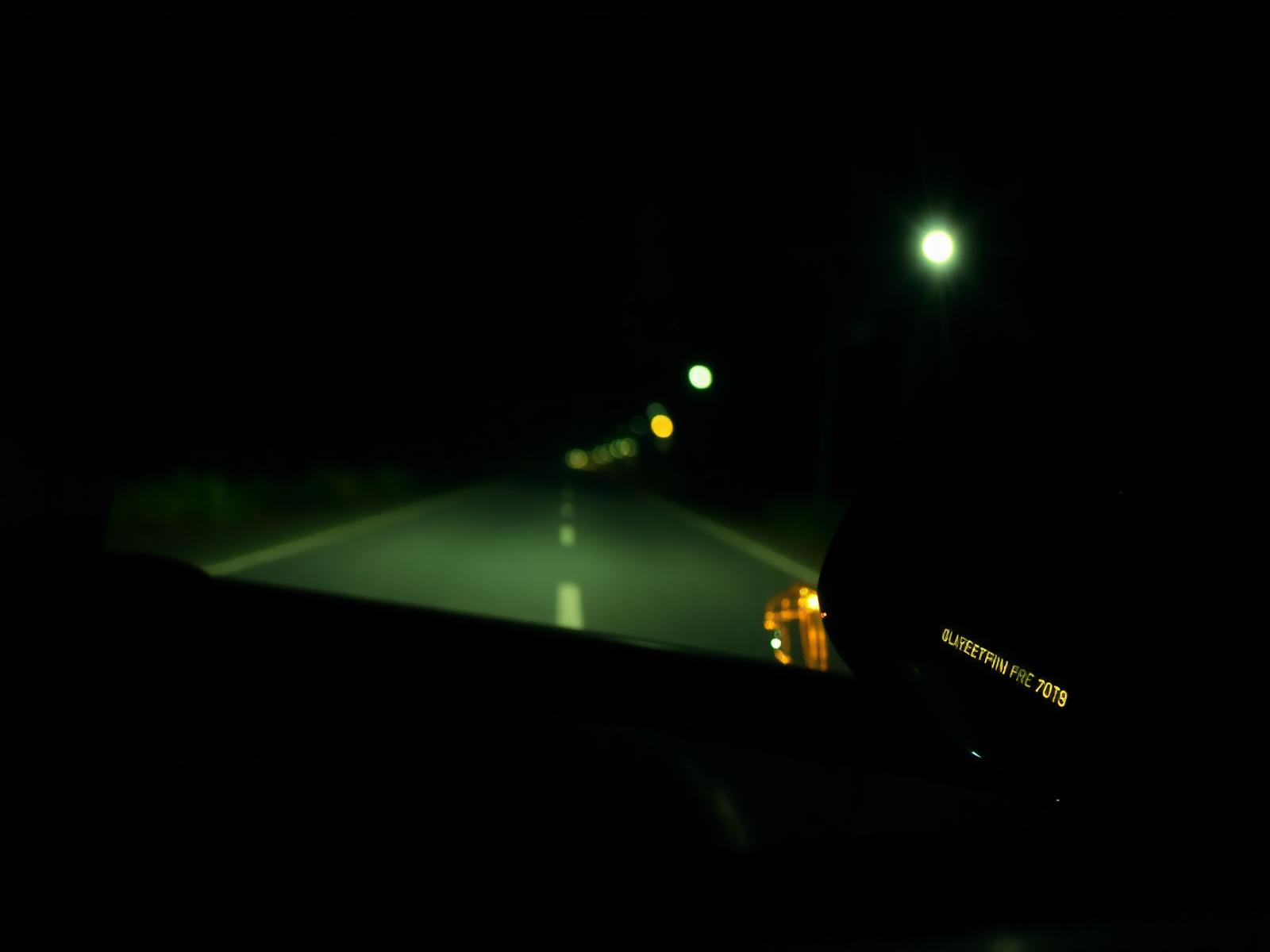 A wet, empty road at night seen from inside a car